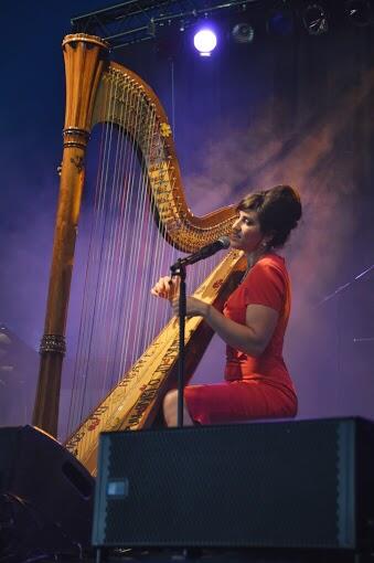 Lucinda Belle singing and playing harp on an outdoor festival stage
